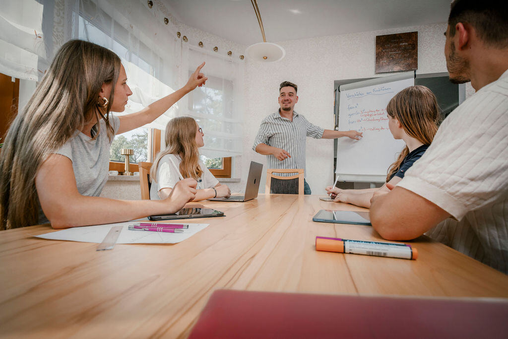 LeviThias Nachhilfe Gruppenunterricht in Zwenkau eine Schülerin meldet sich zwei schauen nachdenklich nach vorne zum lächelnden Lehrer